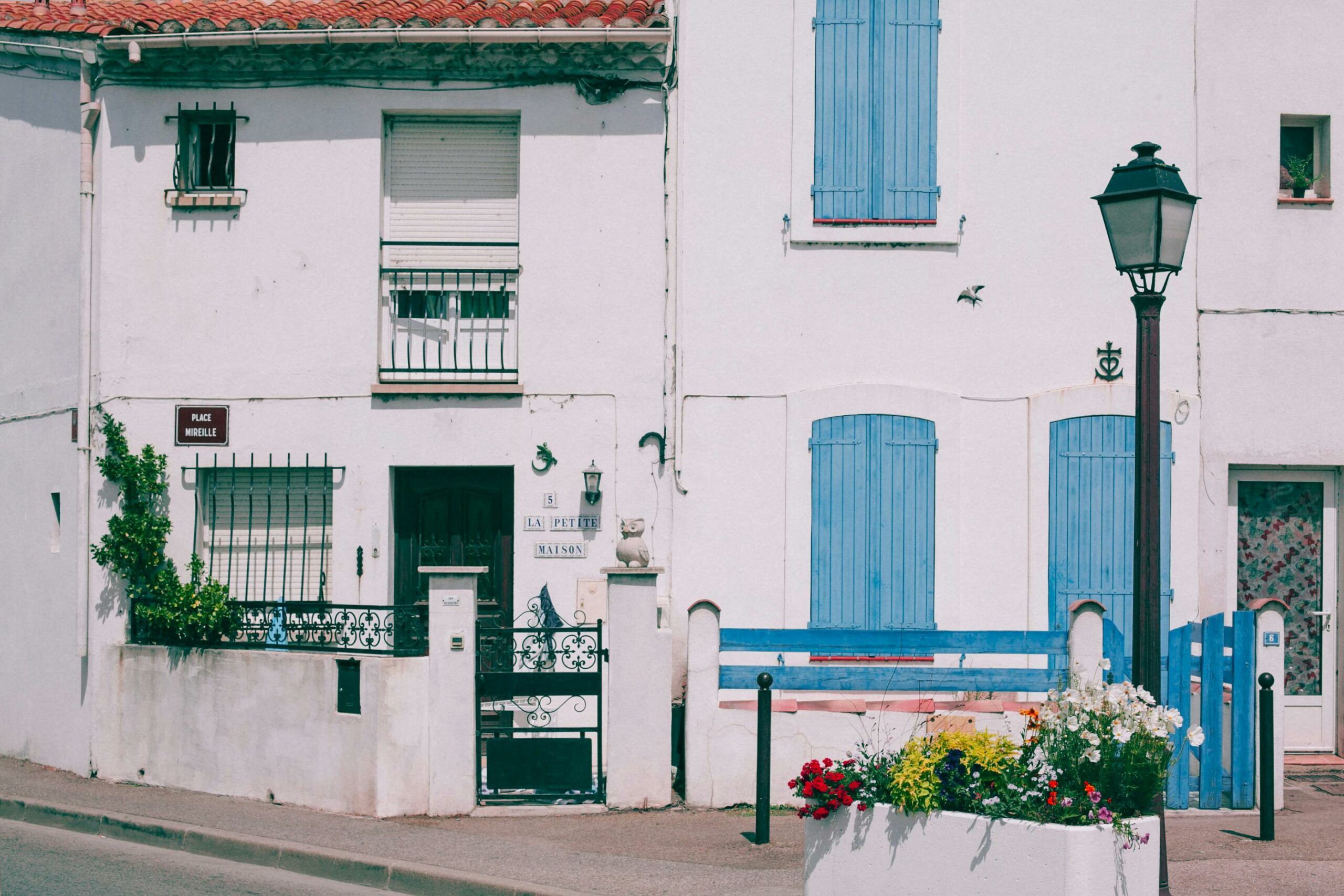 Acceuil A charming facade of a French building with blue shutters, a street lamp, and floral details.