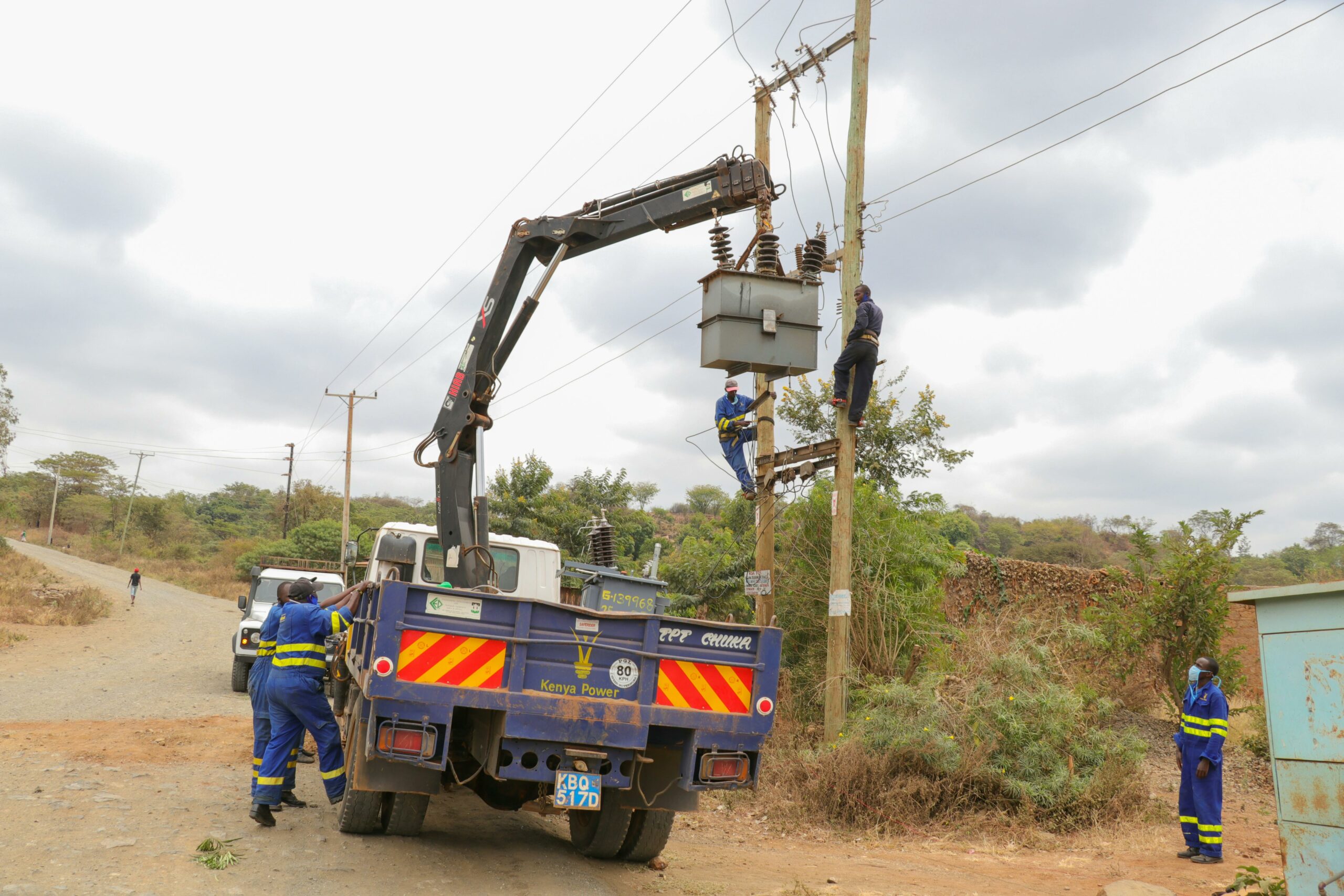 Acceuil Utility workers in protective gear servicing power lines with a truck crane on a rural road.