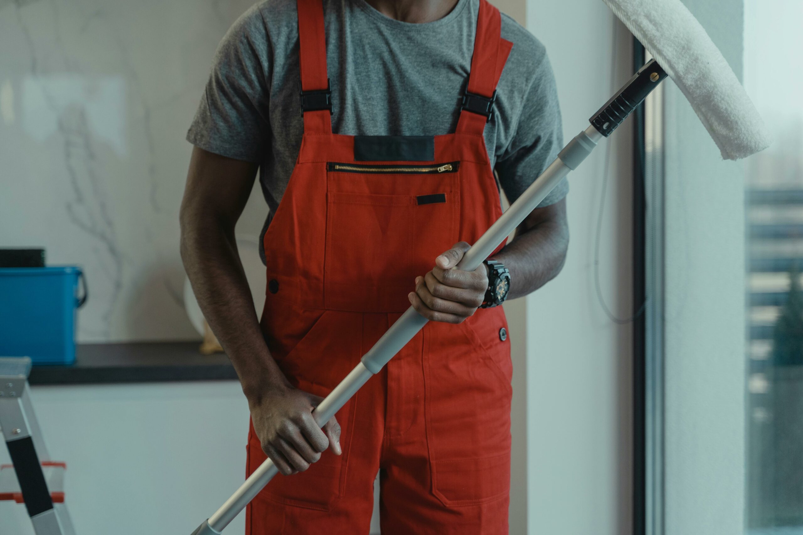 Acceuil A professional cleaner wearing red overalls is holding a mop while cleaning indoors.